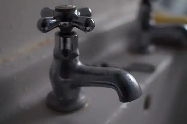 An old chrome basin tap with cross handles above a white sink