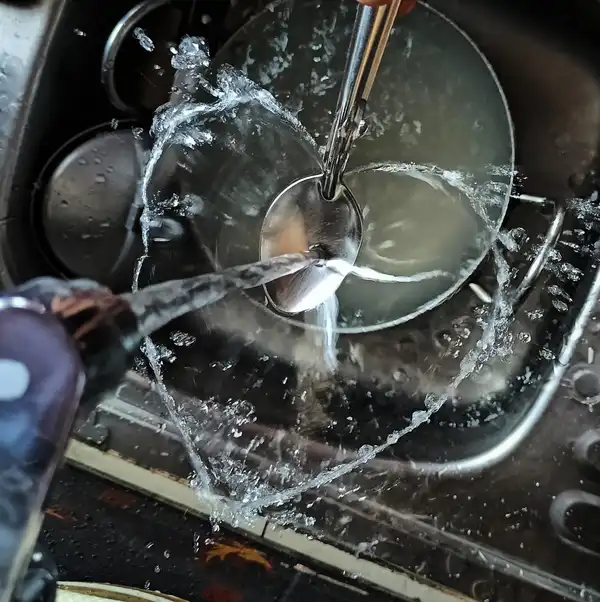 Water from a tap splashing over a spoon in a stainless steel kitchen sink